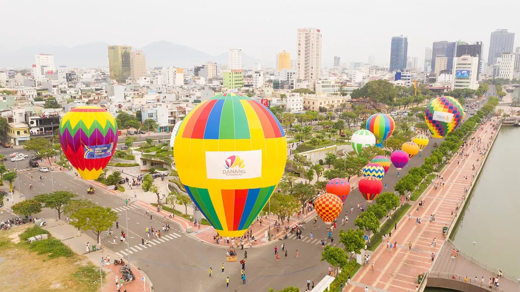 A vibrant hot air balloon floating over the coastal city of Da Nang, with stunning views of the blue ocean, lush greenery, and distant mountains under a clear sky