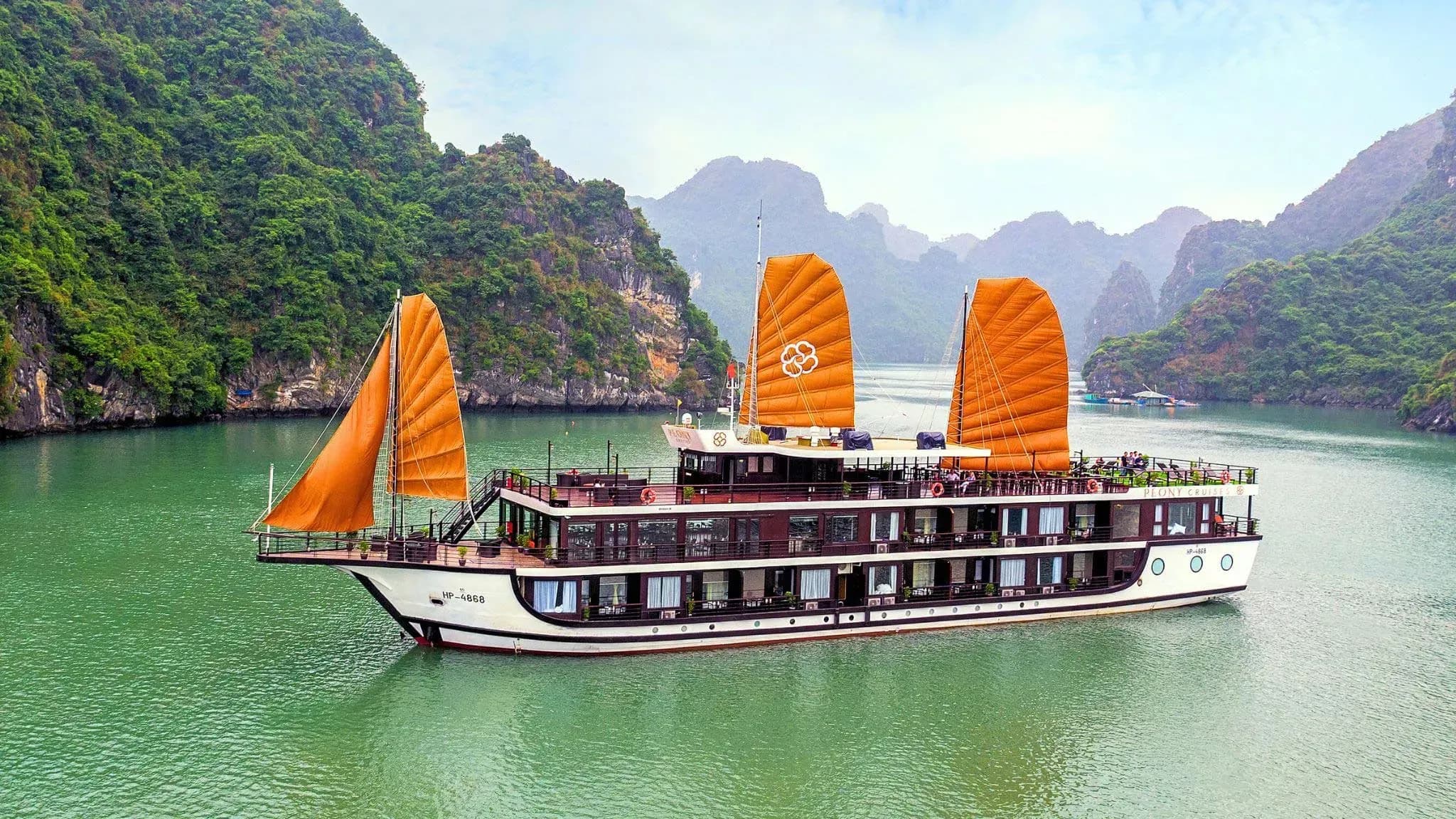 오렌지색의 크루즈는 울창한 석회암 산으로 둘러싸인 Ha Long Bay에 서 있습니다.